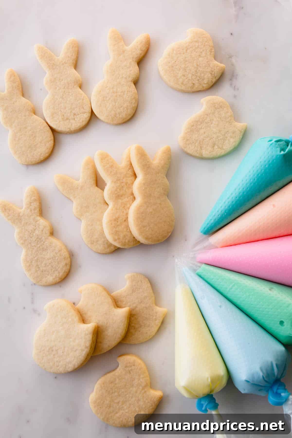 Pastel-colored royal icing in piping bags, laid out next to un-iced Peep and bunny-shaped Easter sugar cookies, ready for decoration.
