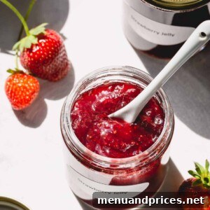 Strawberry jam in a glass jar with a spoon in the jar.
