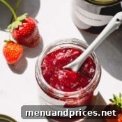 Strawberry jam in a glass jar with a spoon in the jar.