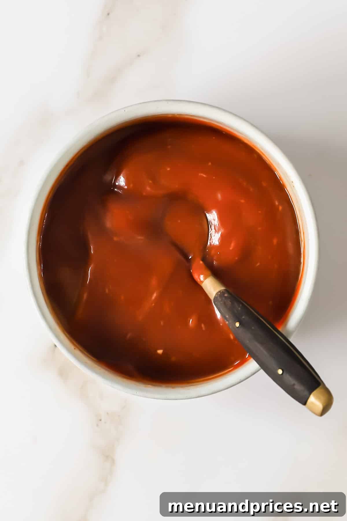 Zesty Prawn Cocktail 7 A small bowl of homemade cocktail sauce with a spoon, showing its smooth texture and vibrant color.