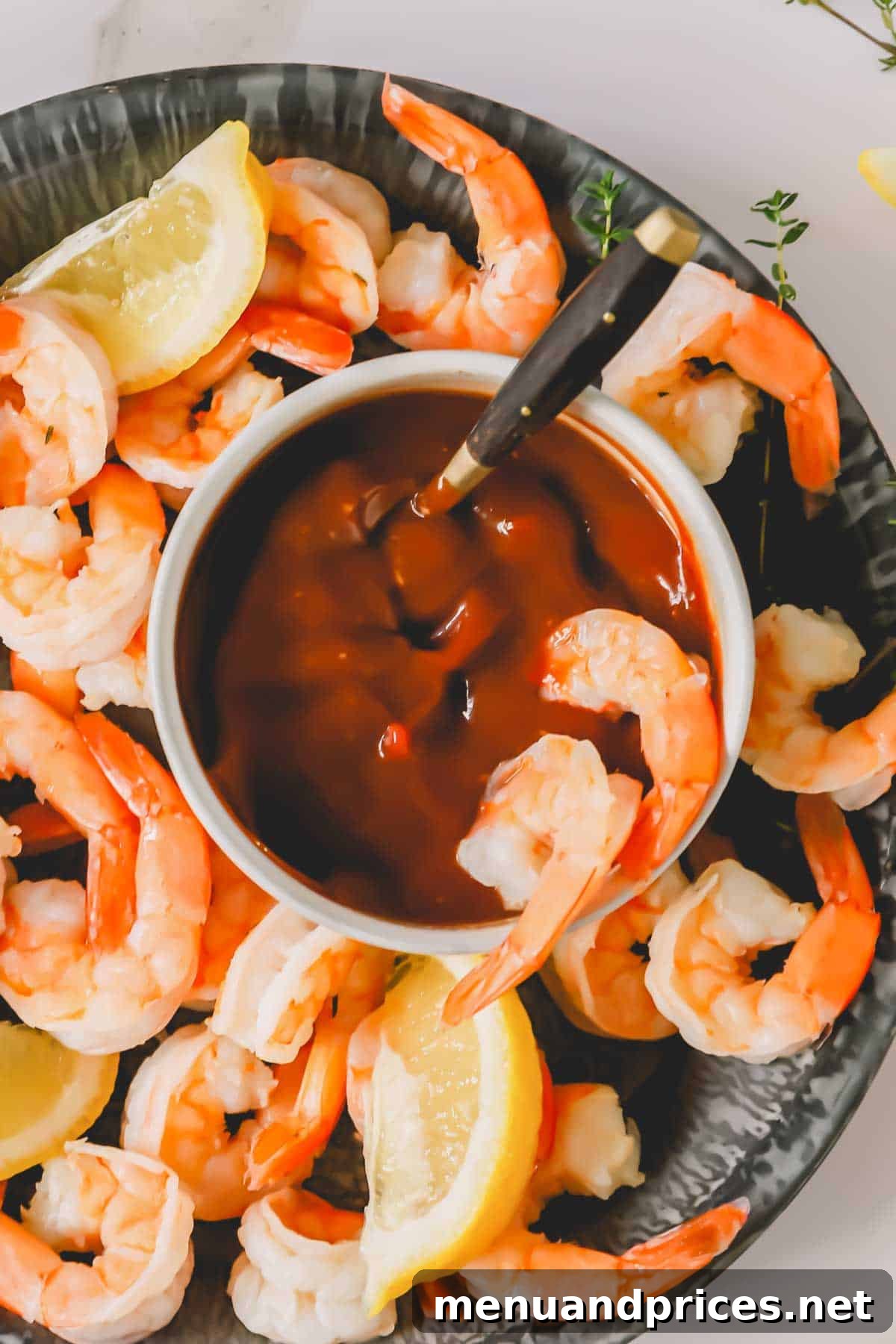Zesty Prawn Cocktail 9 Two succulent shrimp dipped into a bowl of zesty cocktail sauce, resting amidst a platter of chilled shrimp.