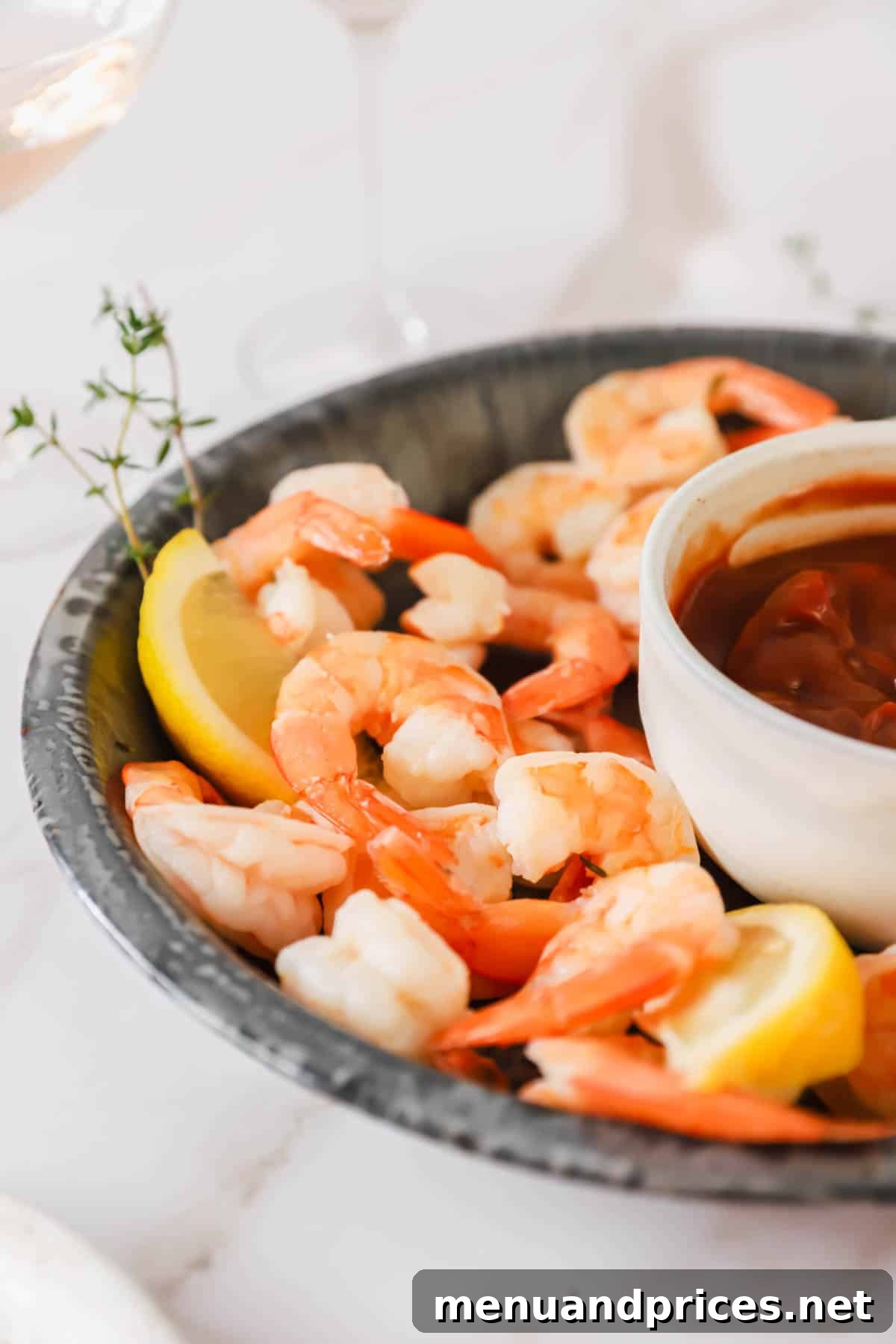 Zesty Prawn Cocktail 10 A stunning side view of a platter filled with perfectly arranged shrimp cocktail, garnished with fresh herbs and lemon wedges, with a bowl of sauce.