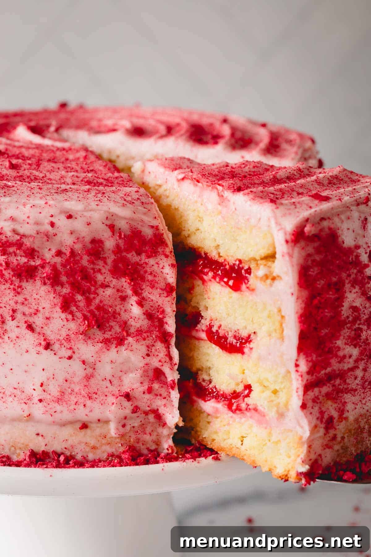 A beautifully decorated raspberry layered sponge cake with rich raspberry frosting and fresh raspberries.