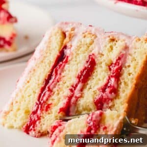 A slice of raspberry layer cake with raspberry jam on a plate with a fork cutting a bite.