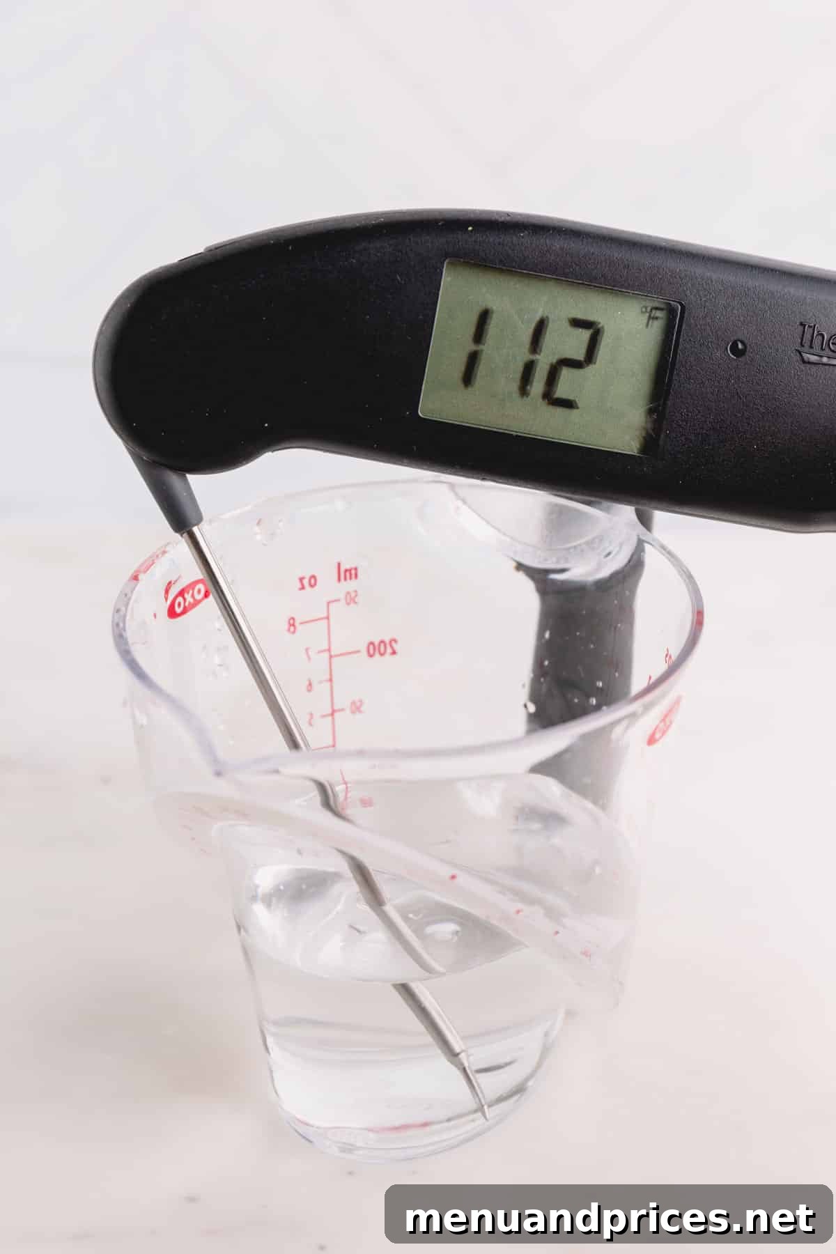 Yeast Essentials: Types and Their Ideal Uses 6 A liquid measuring cup displaying warm water, with an instant-read thermometer accurately indicating a temperature of 112 degrees Fahrenheit, perfect for yeast activation.