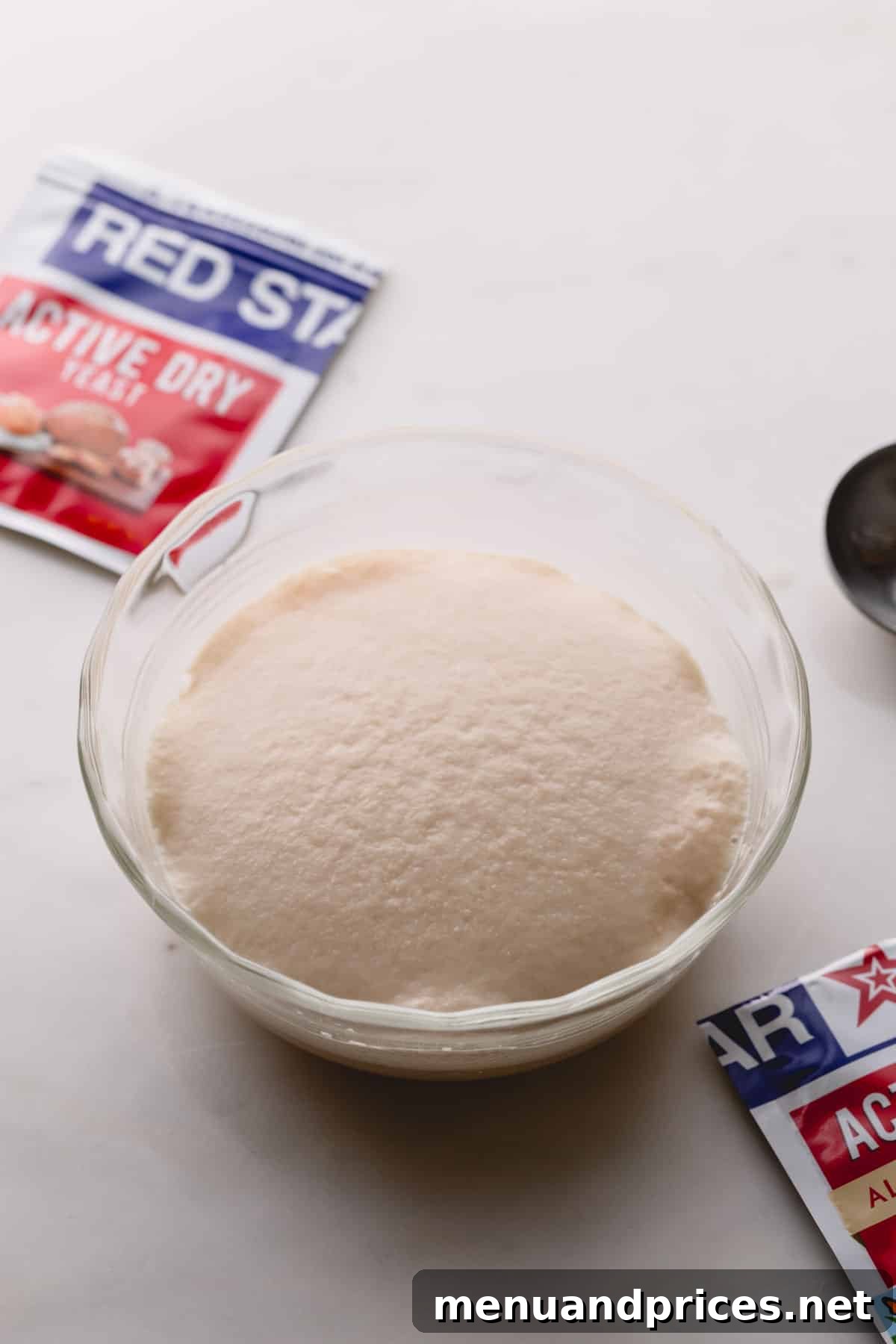 Yeast Essentials: Types and Their Ideal Uses 8 A small glass bowl containing a fully proofed yeast mixture, visibly puffed up and active, with a packet of active dry yeast subtly blurred in the background, signaling success.