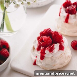 Mini pavlova topped with raspberry whipped cream, raspberry sauce and fresh raspberries.