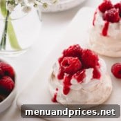Mini pavlova topped with raspberry whipped cream, raspberry sauce and fresh raspberries.