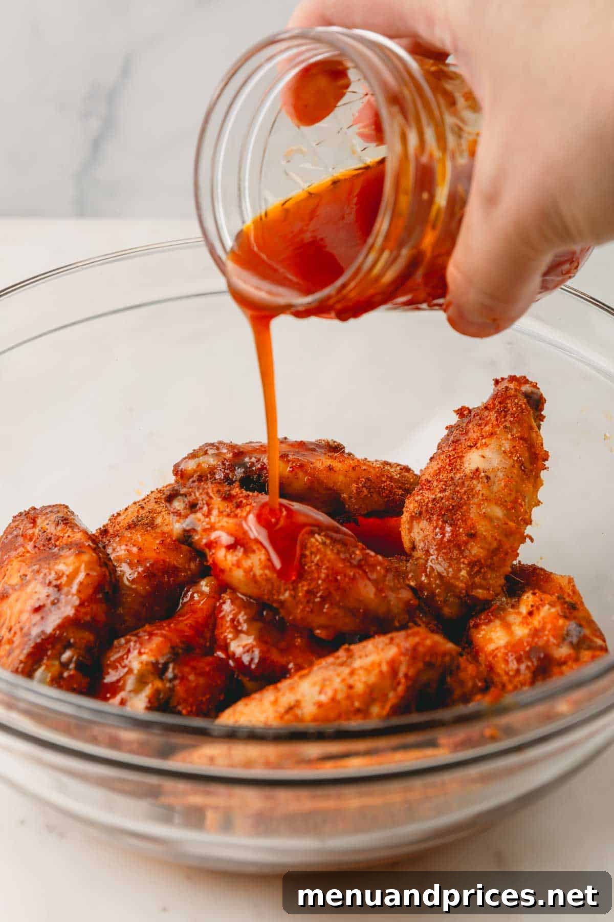 Sticky Sweet Heat Wings 11 Glossy hot honey sauce being poured over a bowl of freshly cooked, seasoned chicken wings.