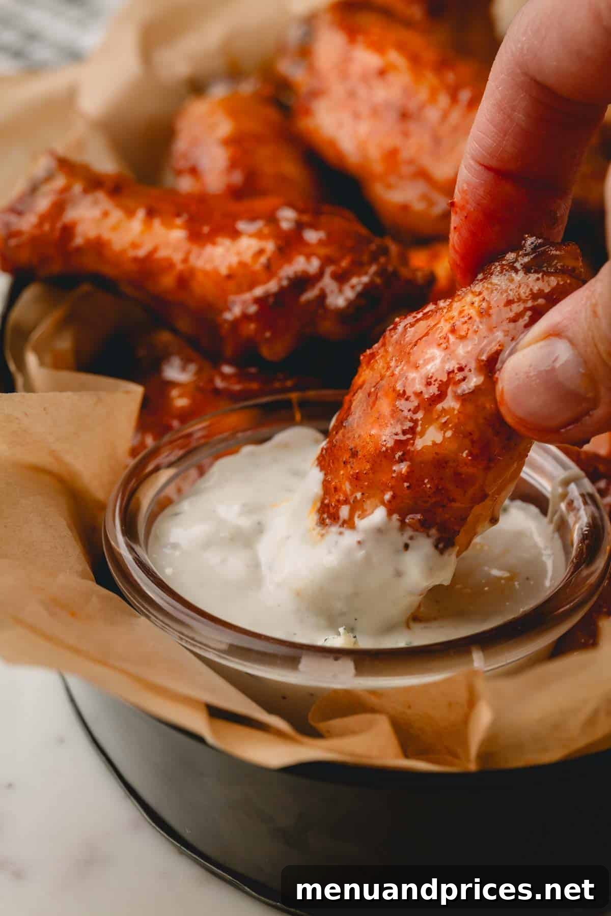 Sticky Sweet Heat Wings 14 A hot honey chicken wing being dipped into a small bowl of creamy Ranch dressing, highlighting a popular serving suggestion.