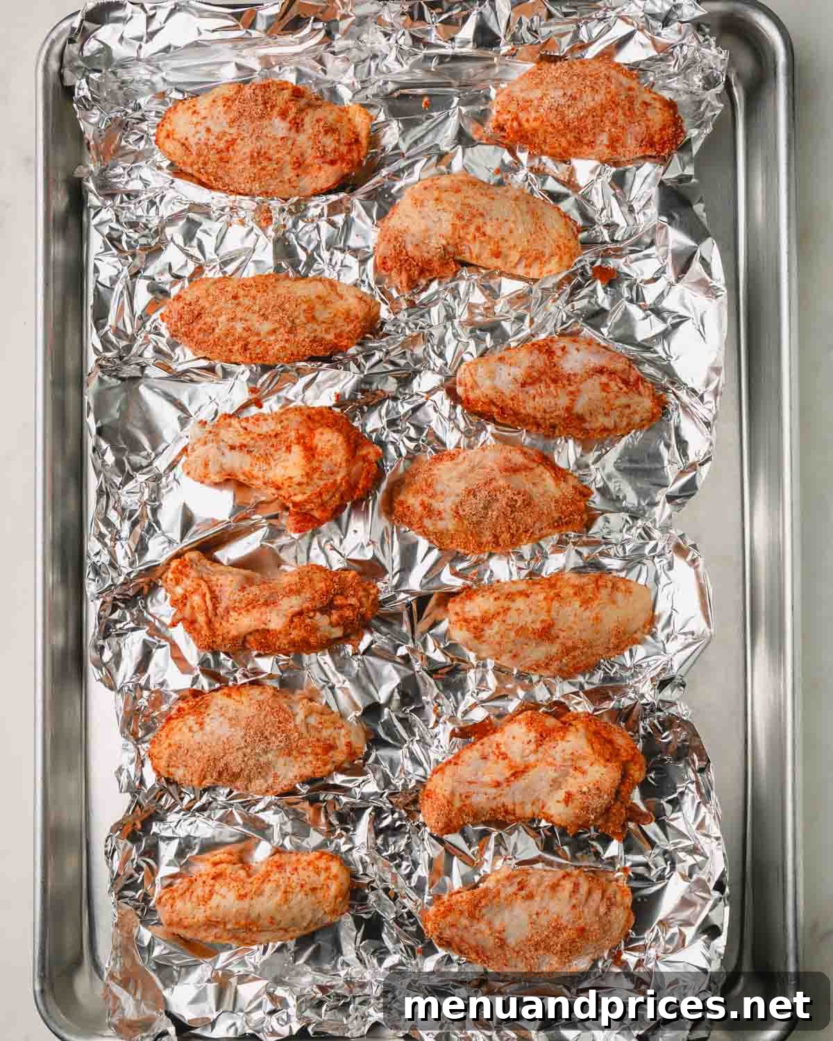 Sticky Sweet Heat Wings 9 Raw seasoned chicken wings meticulously arranged on a wire rack on a baking sheet lined with aluminum foil, ready for the oven.