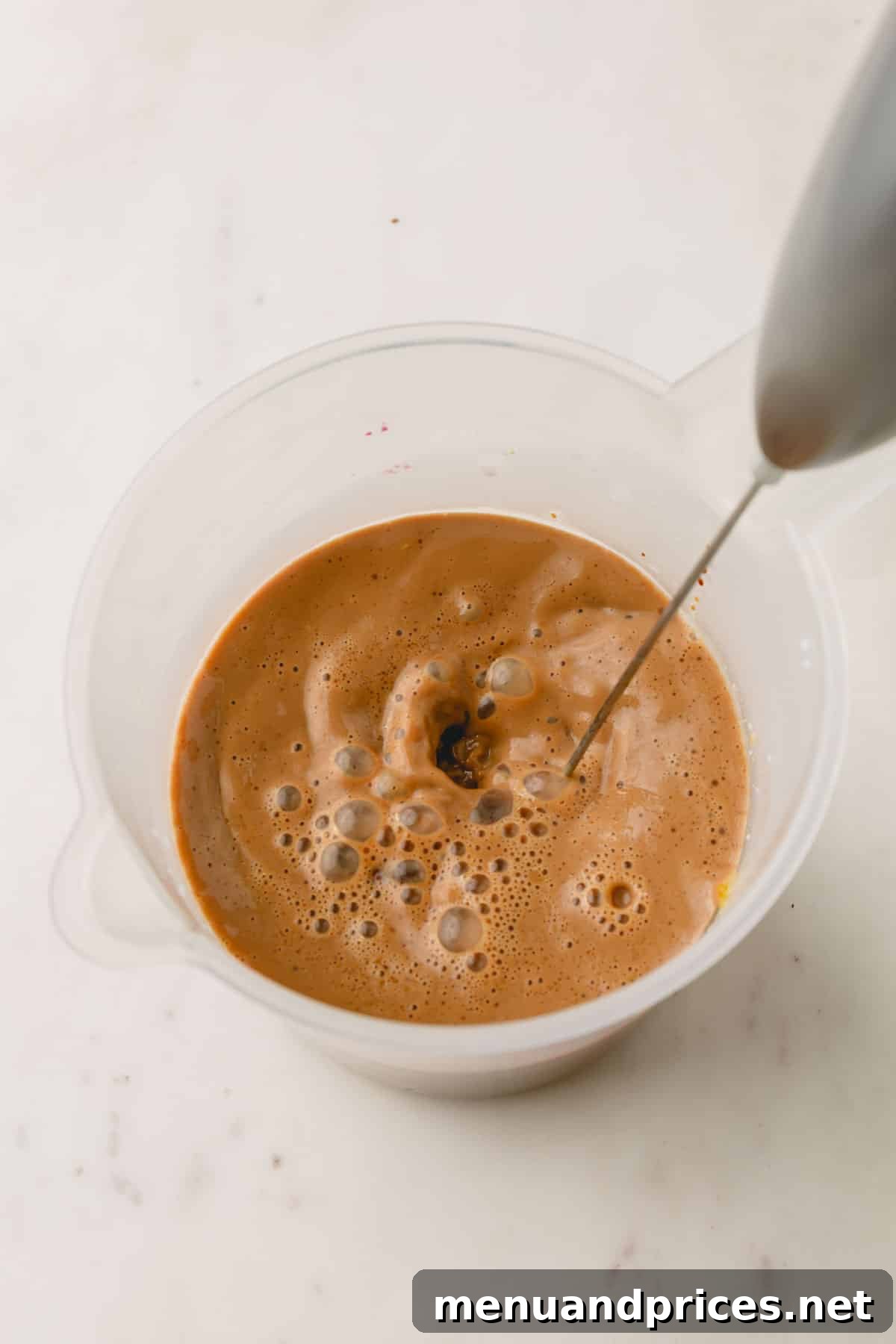 Pistachio latte ingredients being combined in a liquid measuring cup with a milk frother.