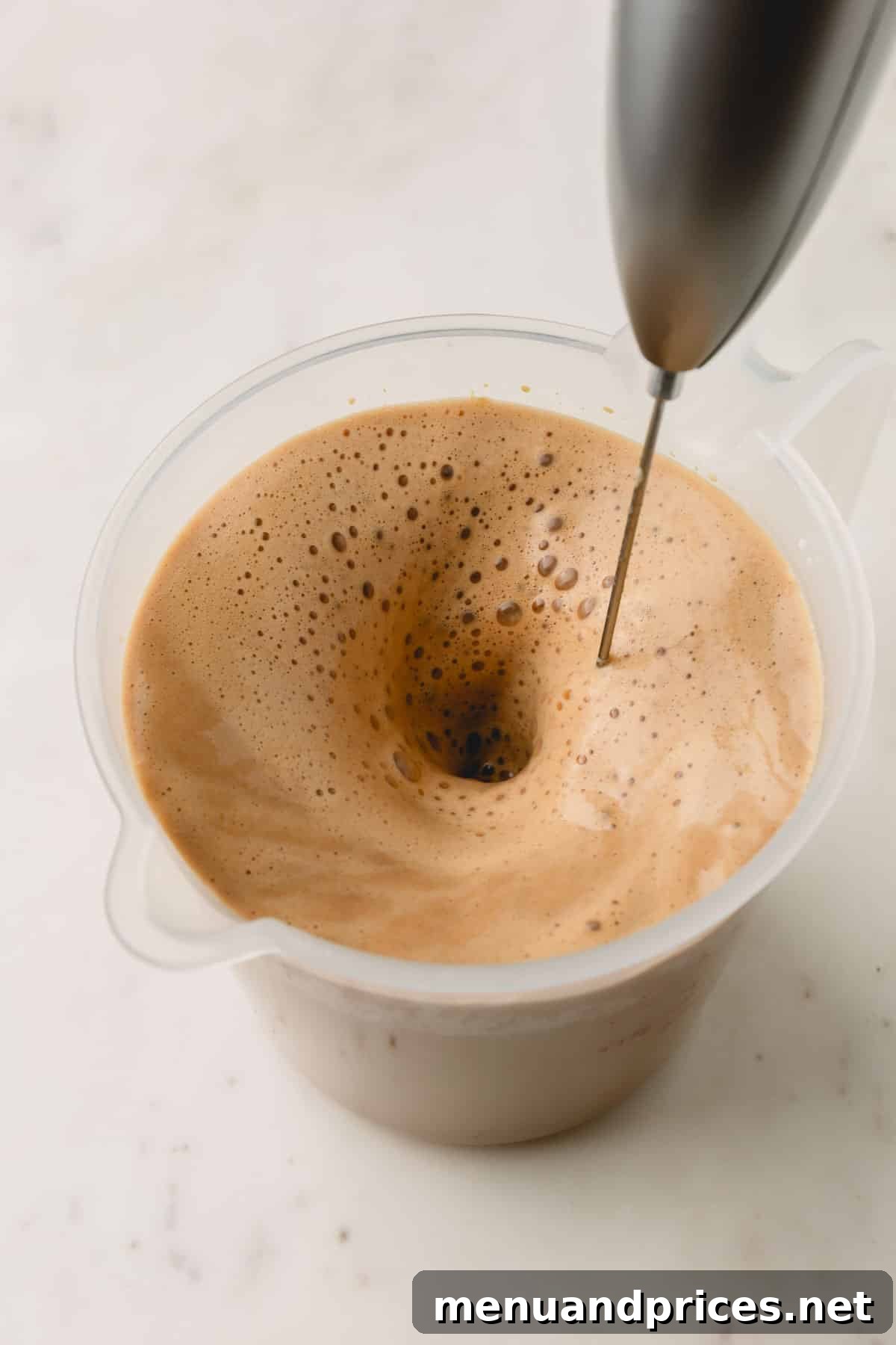 A milk frother frothing a pistachio latte in a liquid measuring cup.