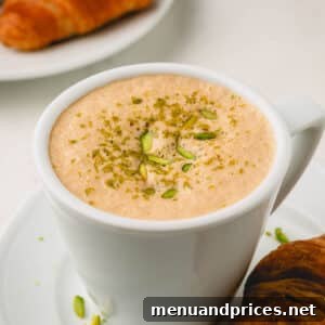 A pistachio latte topped with crushed pistachios on a plate with a croissant.