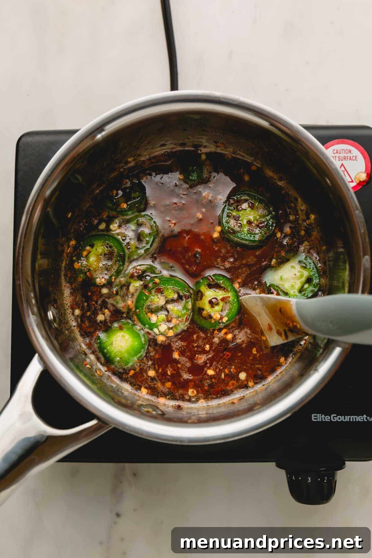 Sweet Heat Honey Formula 5 Honey, red pepper flakes, and jalapeño slices gently simmering in a saucepan on the stove, infusing flavors.