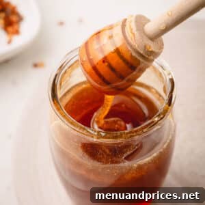A honeycomb lifting hot honey from a jar.