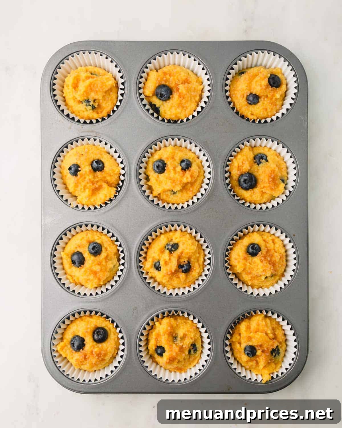 Moist Almond Flour Blueberry Muffins 11 Twelve unbaked almond flour blueberry muffins, topped with demerara sugar, neatly arranged in a muffin pan before going into the oven.