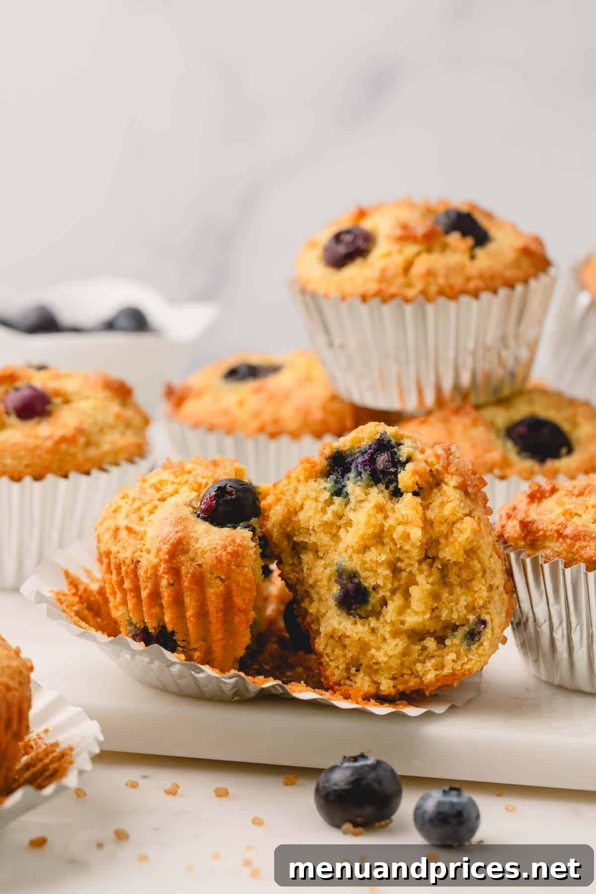 Moist Almond Flour Blueberry Muffins 14 A perfectly baked almond flour blueberry muffin, split in half to show its soft, fruit-filled interior, resting on its muffin liner.