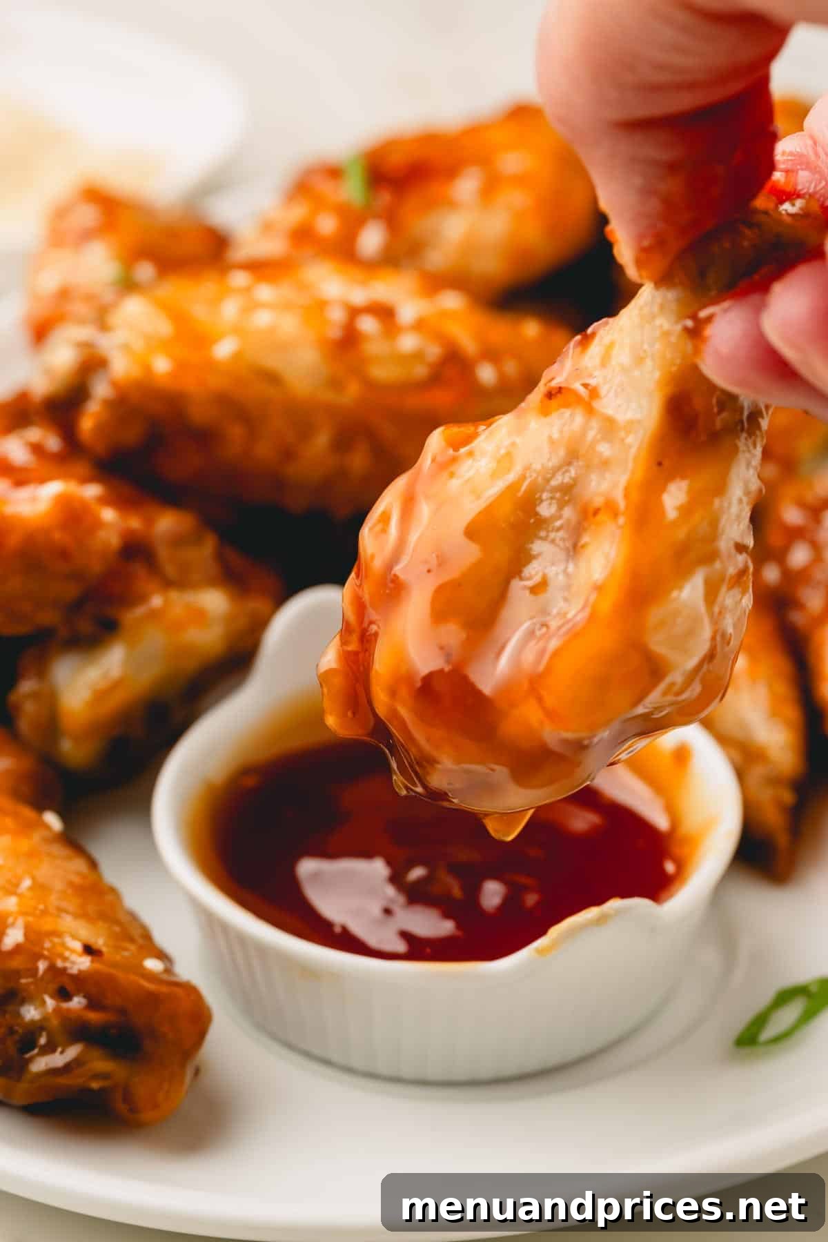 Sticky Honey Teriyaki 4 A succulent chicken wing being generously dipped into a small ramekin of luscious honey teriyaki sauce.