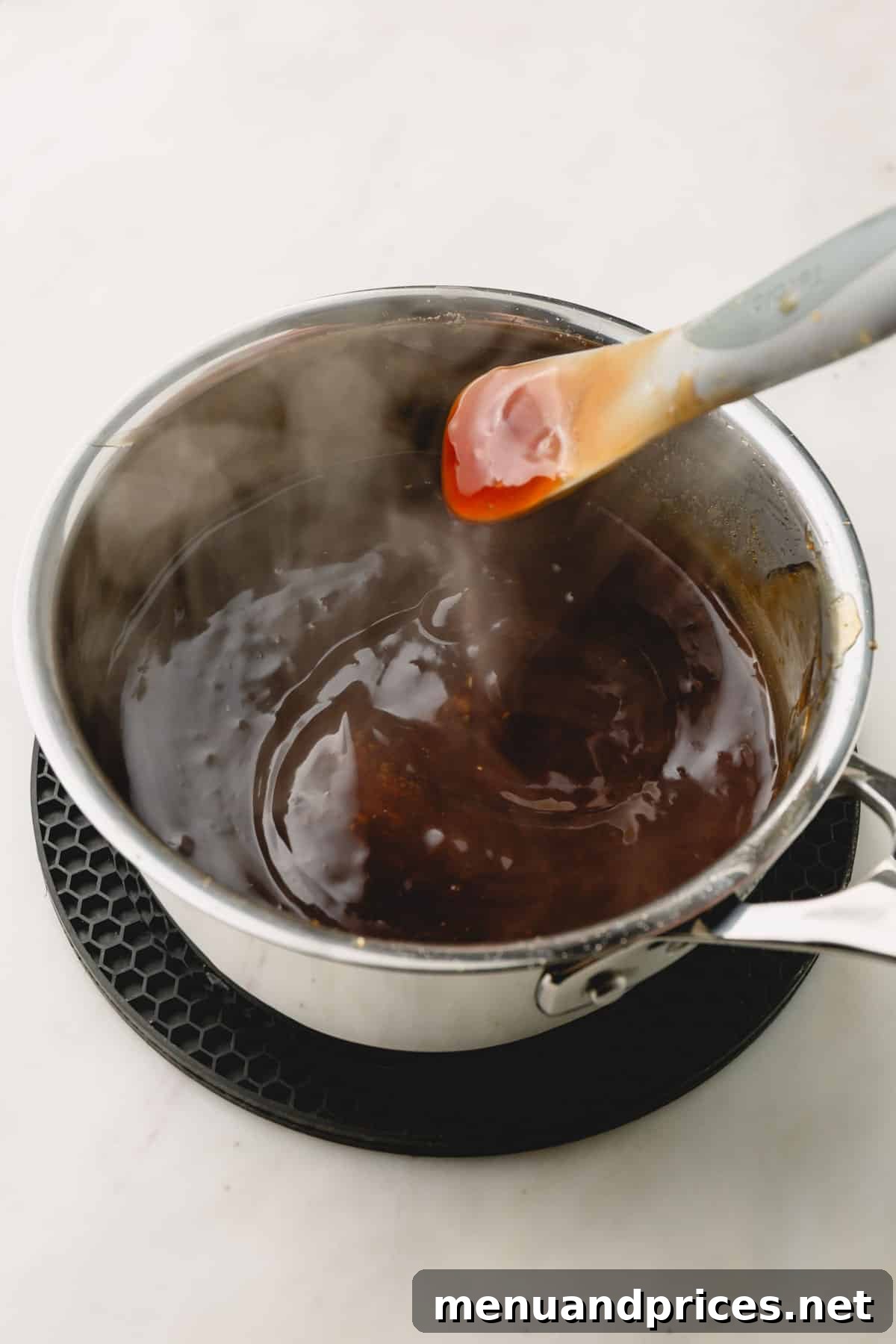 Sticky Honey Teriyaki 9 A close-up of honey teriyaki sauce being expertly stirred in a saucepan, highlighting its smooth, glossy texture.