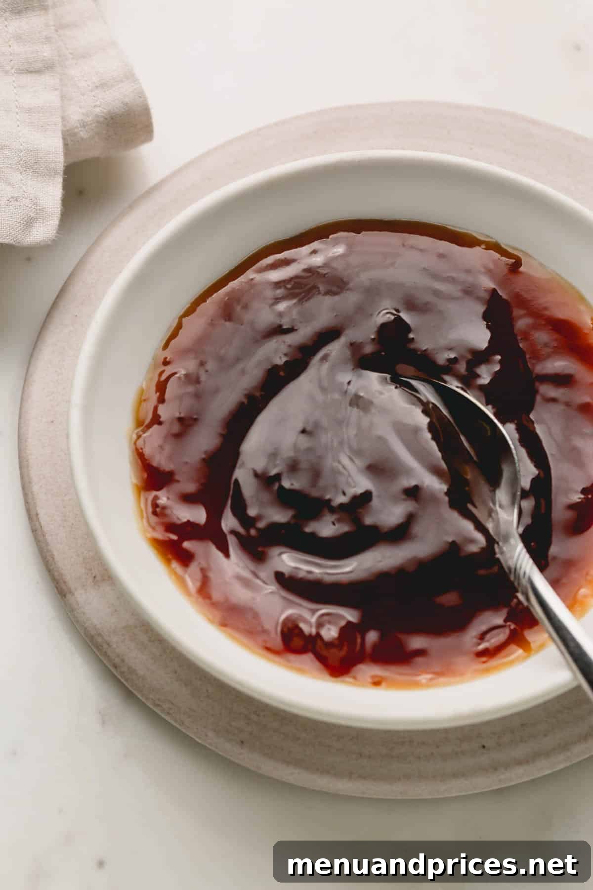Sticky Honey Teriyaki 10 A white bowl filled with glossy homemade honey teriyaki sauce, featuring a spoon invitingly dipped into it.