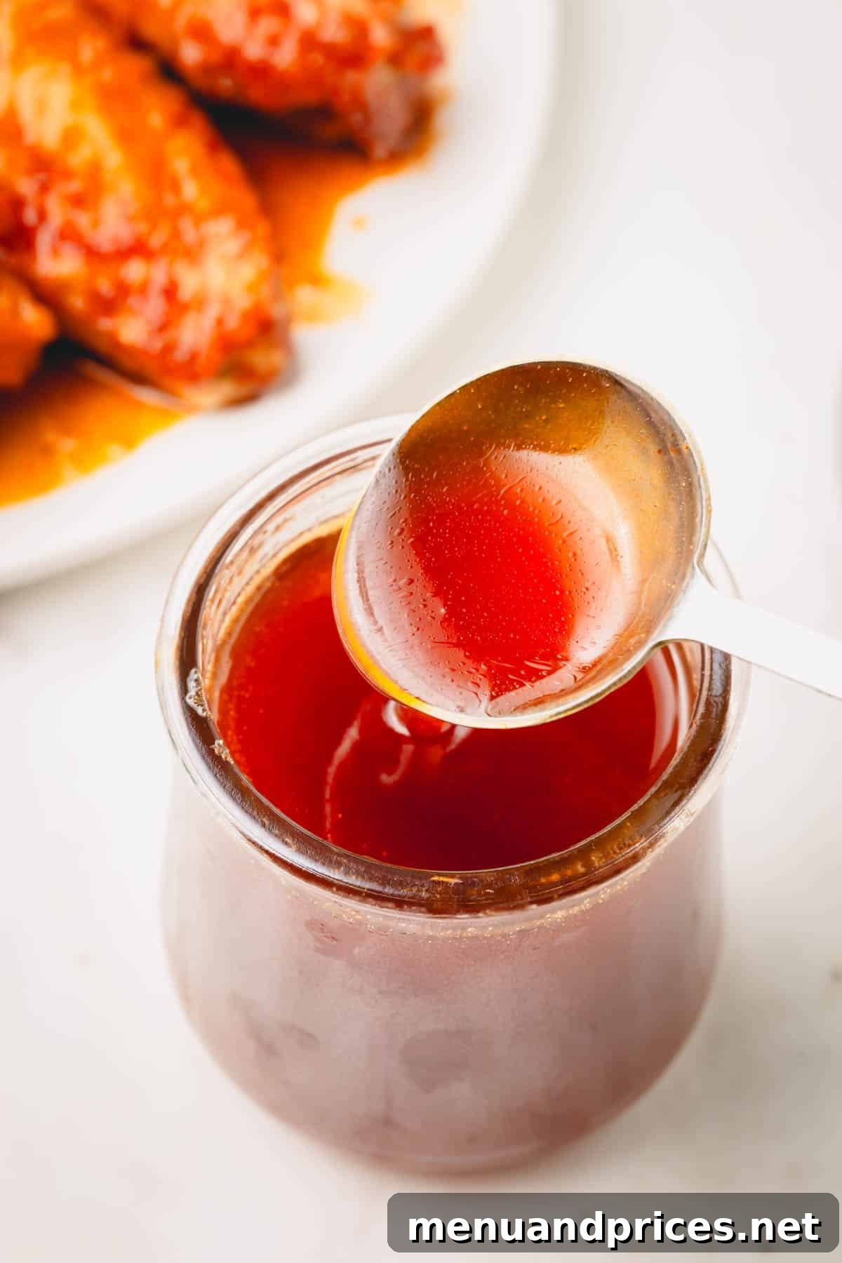Golden Blaze Drizzle 9 A close-up of a spoon lifting a generous scoop of hot honey sauce from a glass jar, highlighting its rich texture and color.