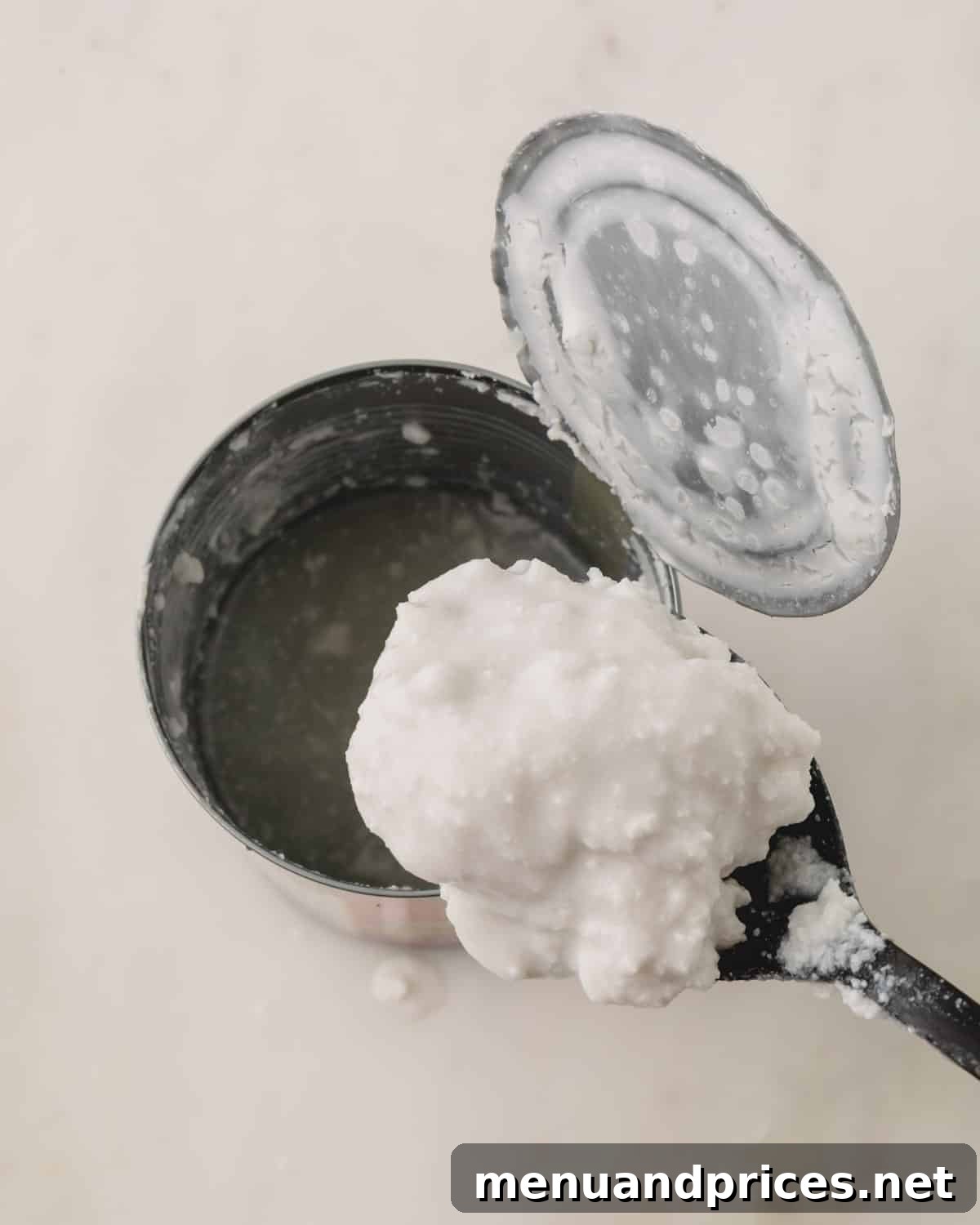 Strawberry Silk Dairy Free Ganache 5 A spoon lifting a rich, thick scoop of coconut cream from a can, highlighting its ideal consistency.