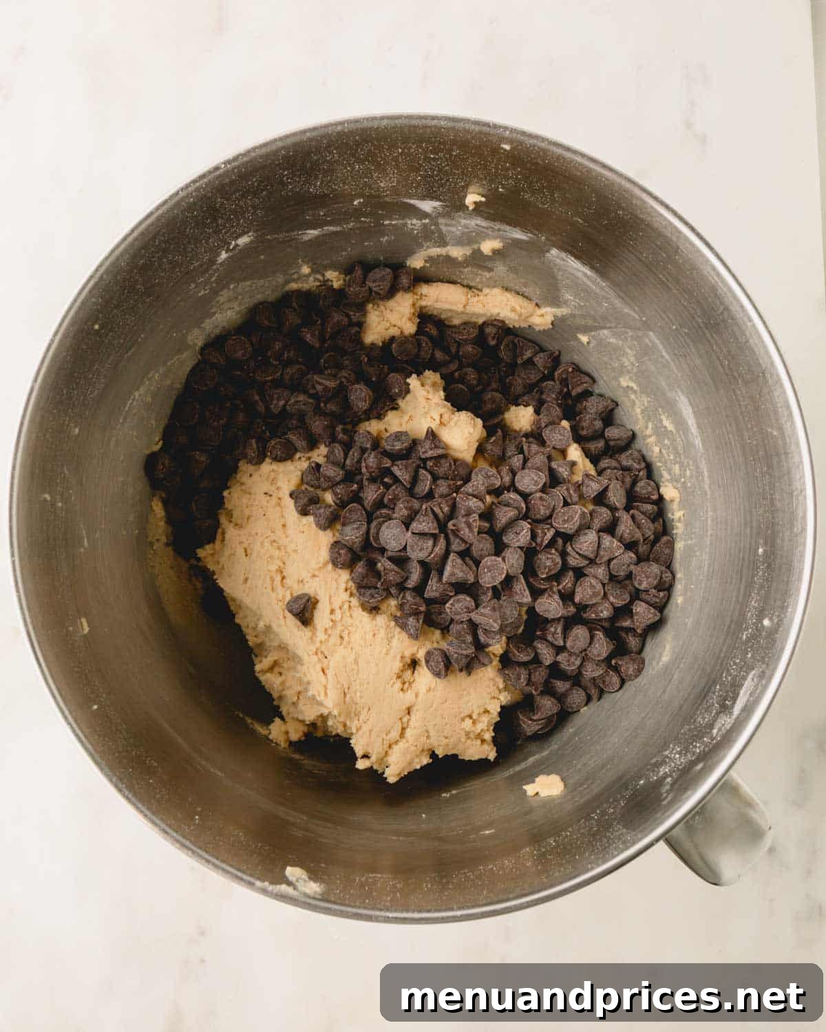 Decadent Thick and Chewy Chocolate Chip Cookies 12 A bowl of cookie dough with a generous amount of chocolate chips sprinkled on top, ready to be folded in.
