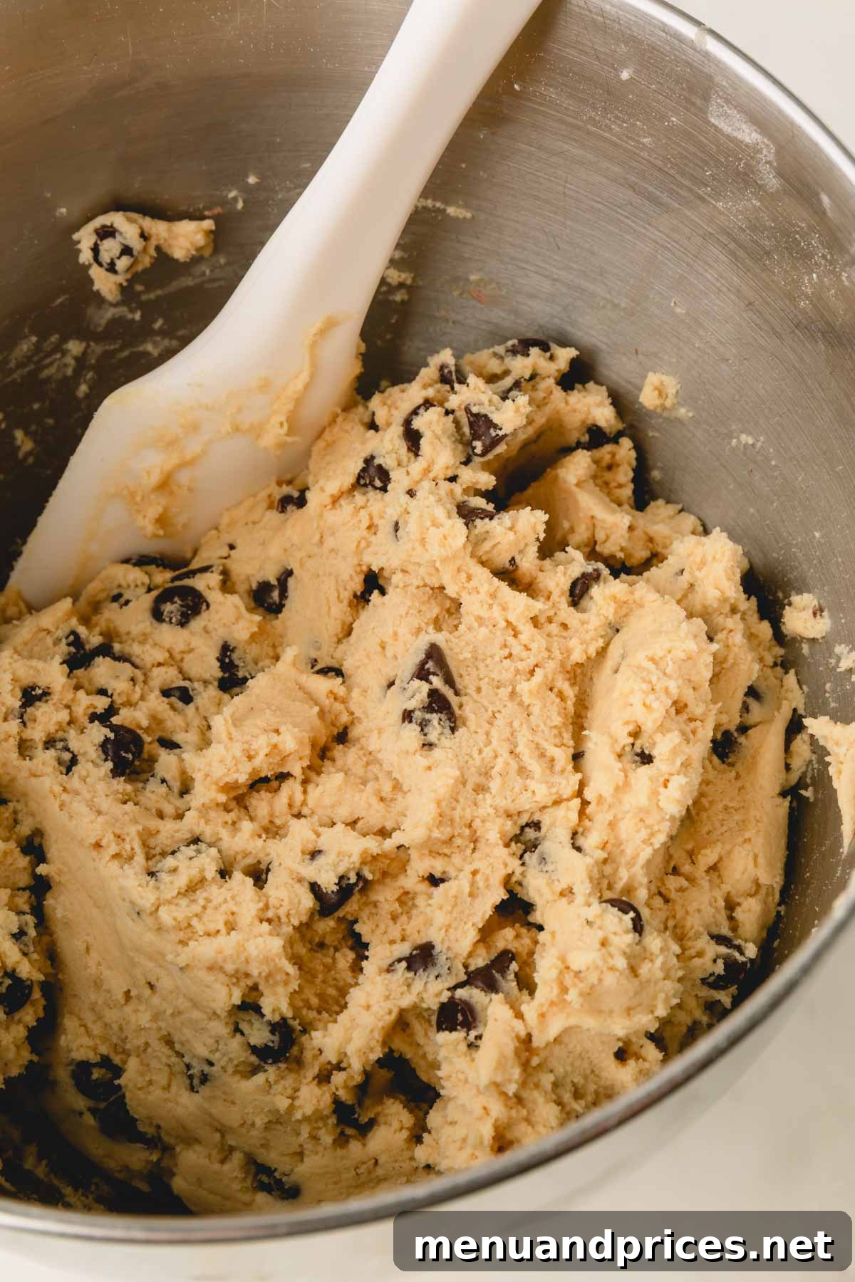 Decadent Thick and Chewy Chocolate Chip Cookies 13 A bowl of chocolate chip cookie dough with a spatula sticking out, indicating the chips have been folded in.
