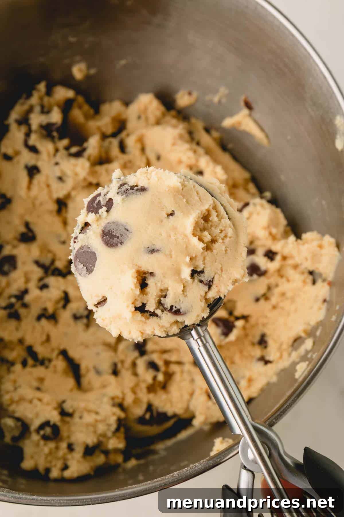 Decadent Thick and Chewy Chocolate Chip Cookies 14 A cookie scoop full of chocolate chip cookie dough, held over the main bowl of dough.