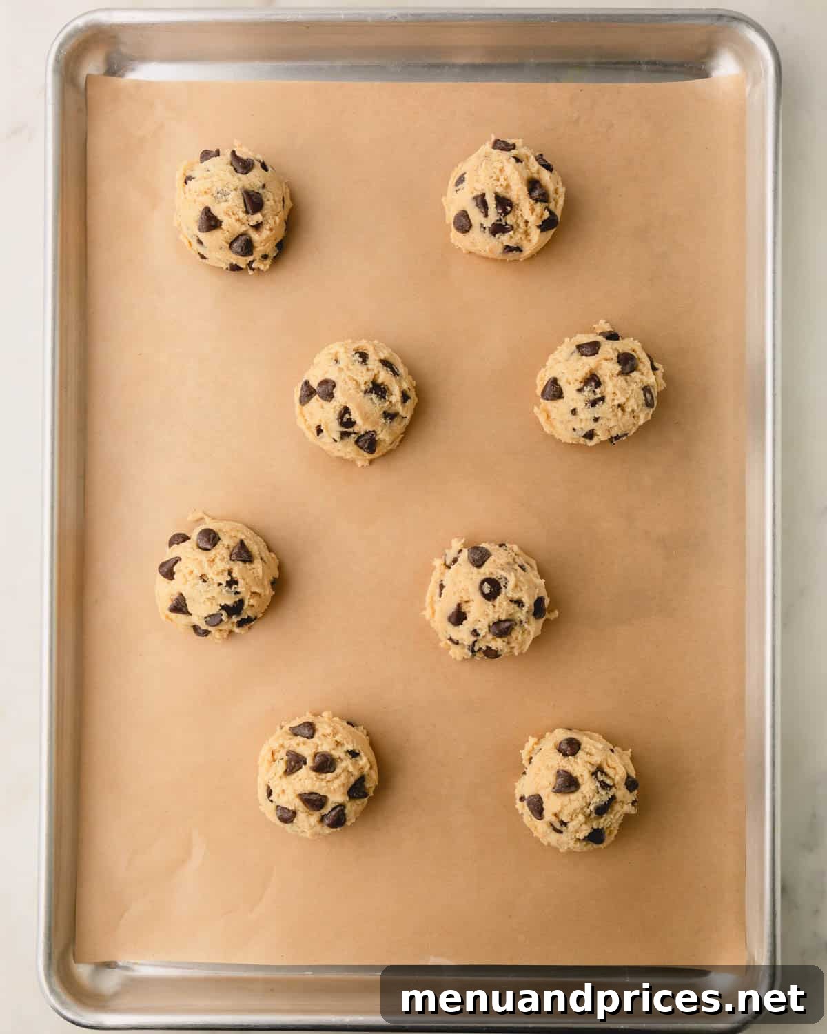 Decadent Thick and Chewy Chocolate Chip Cookies 15 Raw chocolate chip cookie dough balls evenly spaced on a parchment paper-lined baking sheet.