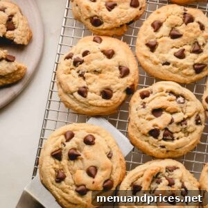 Thick and chewy chocolate chip cookies on a wire rack, a spatula under one.
