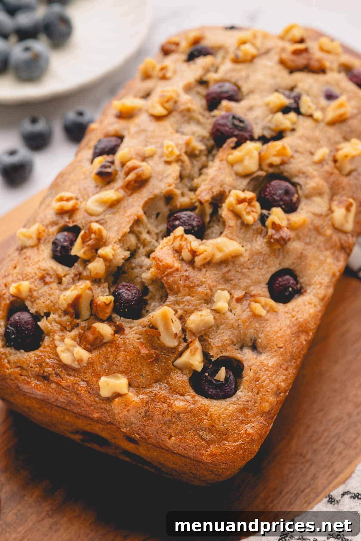 Golden Blueberry Banana Nut Loaf 2 A beautifully baked loaf of blueberry banana bread, garnished with fresh blueberries and walnuts, resting on a rustic wooden surface.