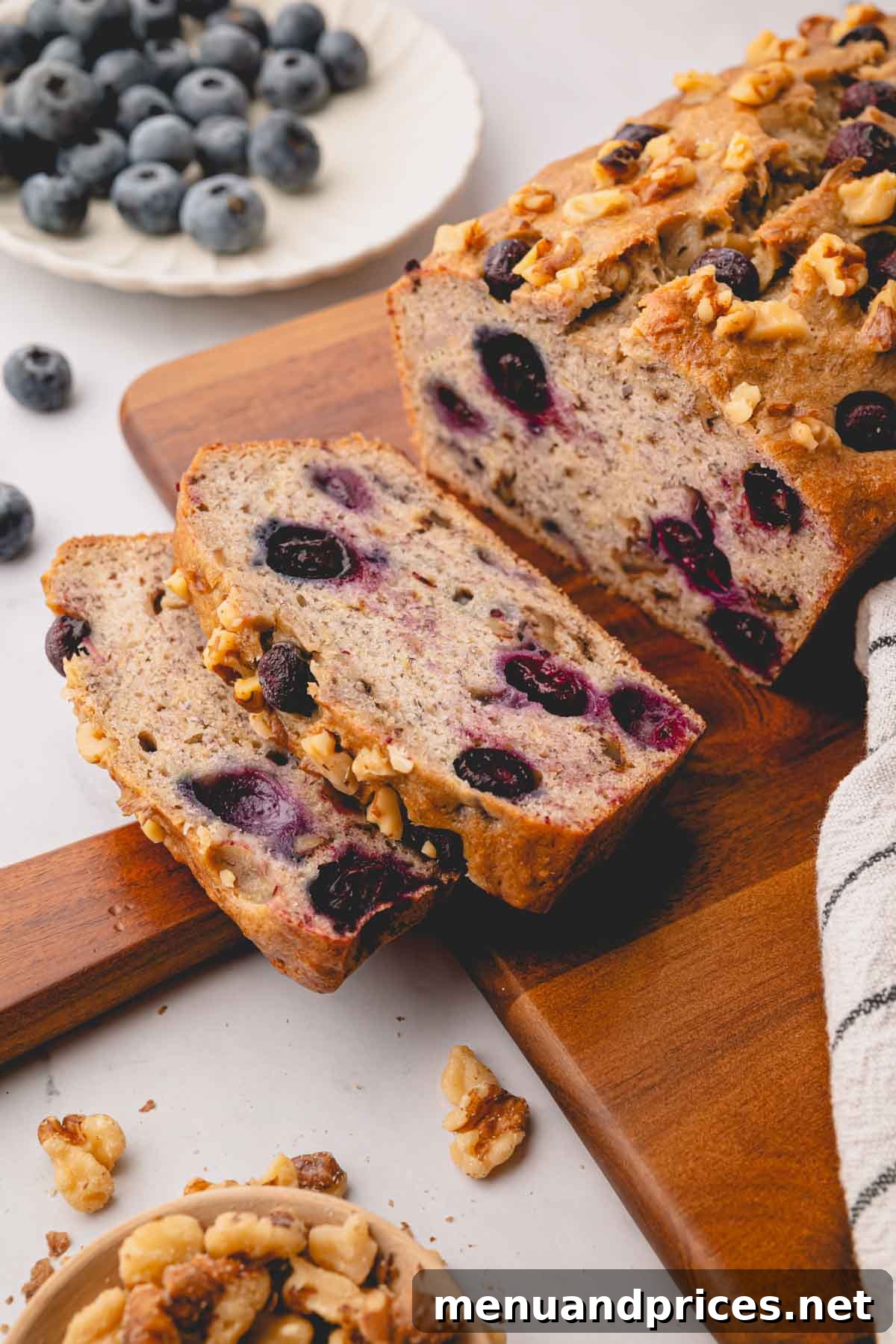 Golden Blueberry Banana Nut Loaf 3 A freshly baked loaf of blueberry banana nut bread on a wooden cutting board, with two perfectly sliced pieces ready to be enjoyed.