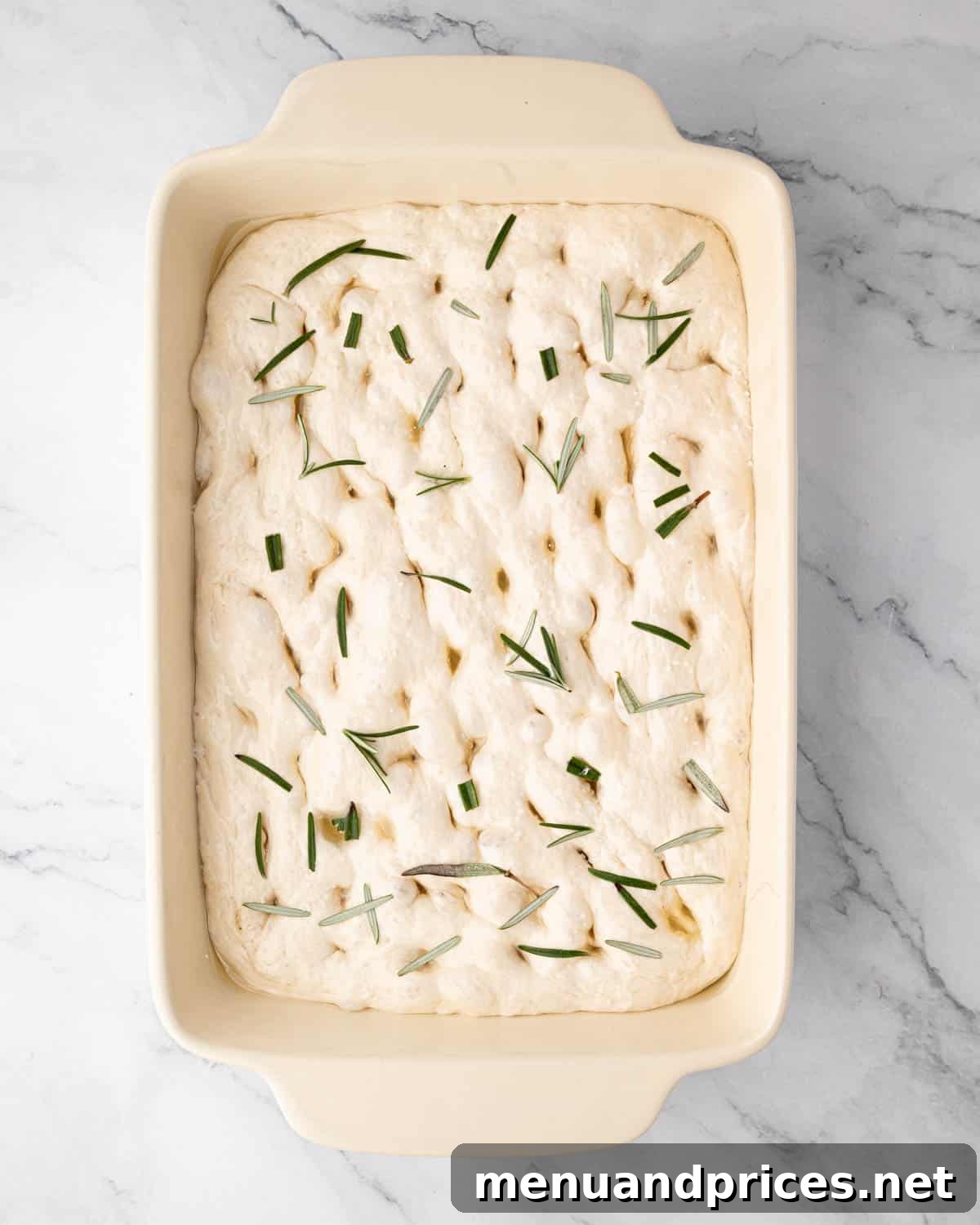 Foolproof Homemade Focaccia 14 Raw focaccia dough meticulously dimpled and adorned with fresh rosemary sprigs and flaky sea salt, ready to be baked.