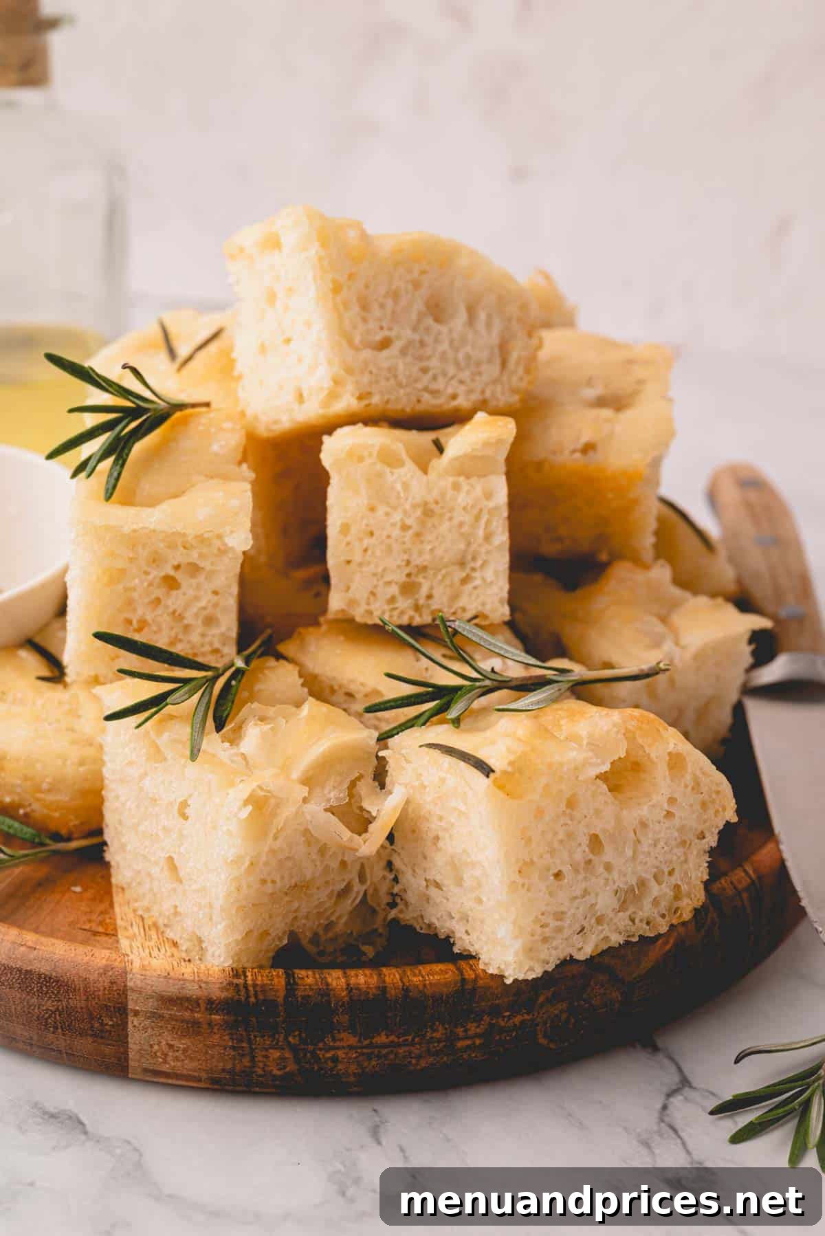 Foolproof Homemade Focaccia 3 Neatly stacked squares of perfectly baked rosemary focaccia bread, presented on an elegant wooden plate, highlighting its golden crust and inviting texture.