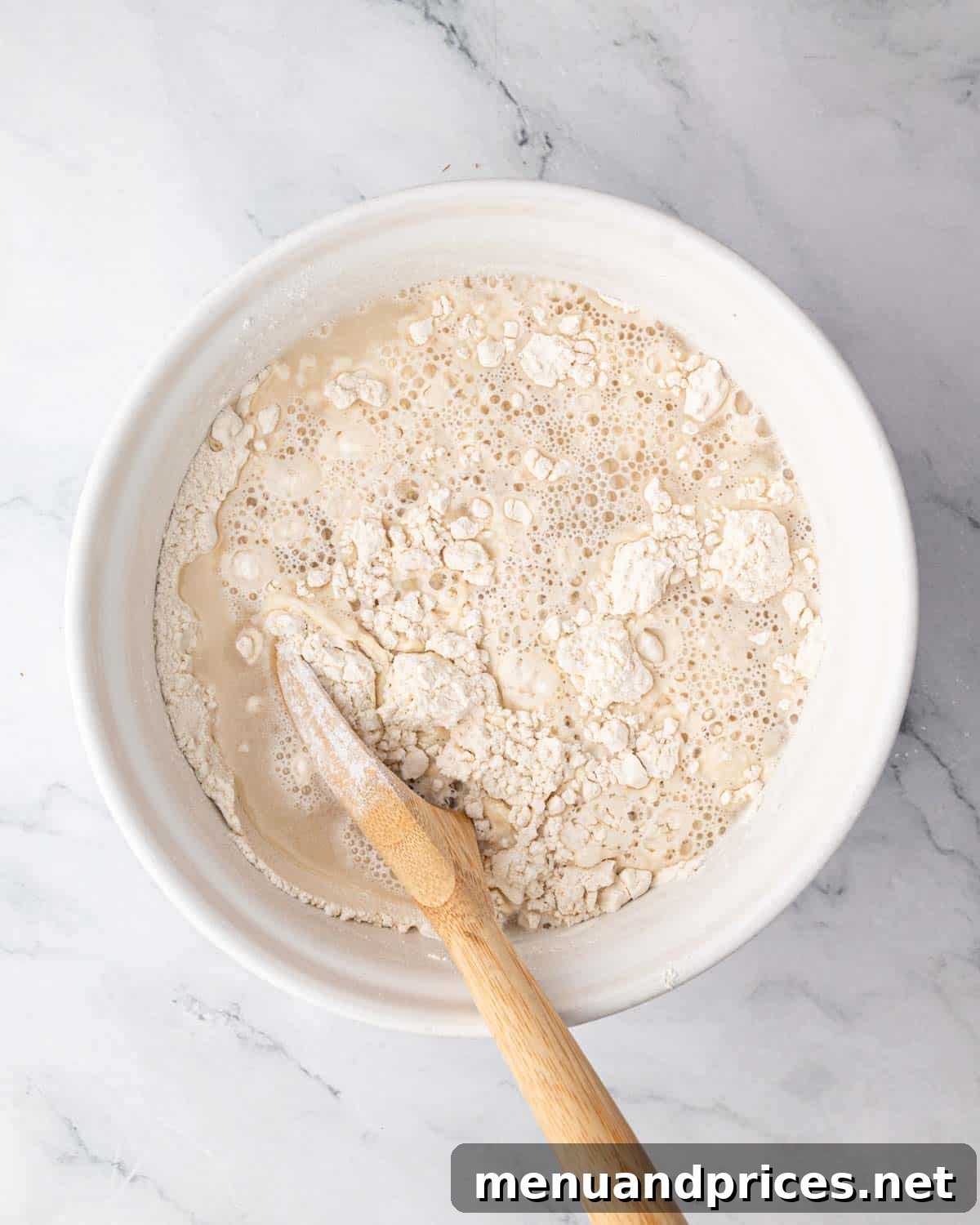 Foolproof Homemade Focaccia 6 A close-up shot of dry ingredients and wet ingredients for focaccia bread being gently mixed together in a bowl, forming a shaggy dough.