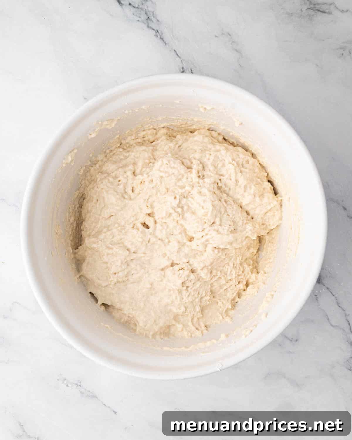 Foolproof Homemade Focaccia 7 Focaccia bread dough in its initial shaggy state, resting in a white mixing bowl after the first mix, covered for hydration.