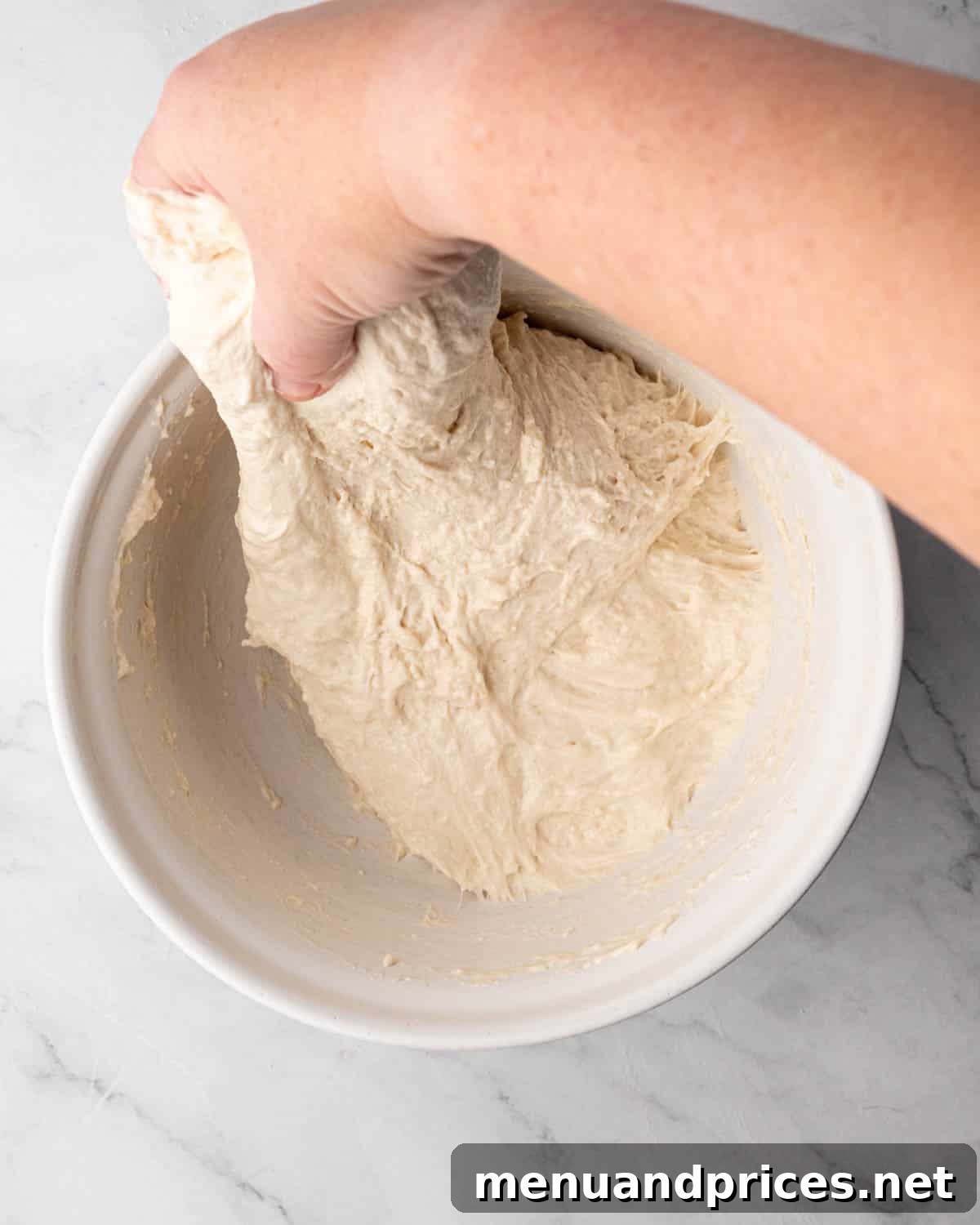 Foolproof Homemade Focaccia 8 A hand gently performing a stretch-and-fold on overnight focaccia bread dough, illustrating the technique for gluten development.