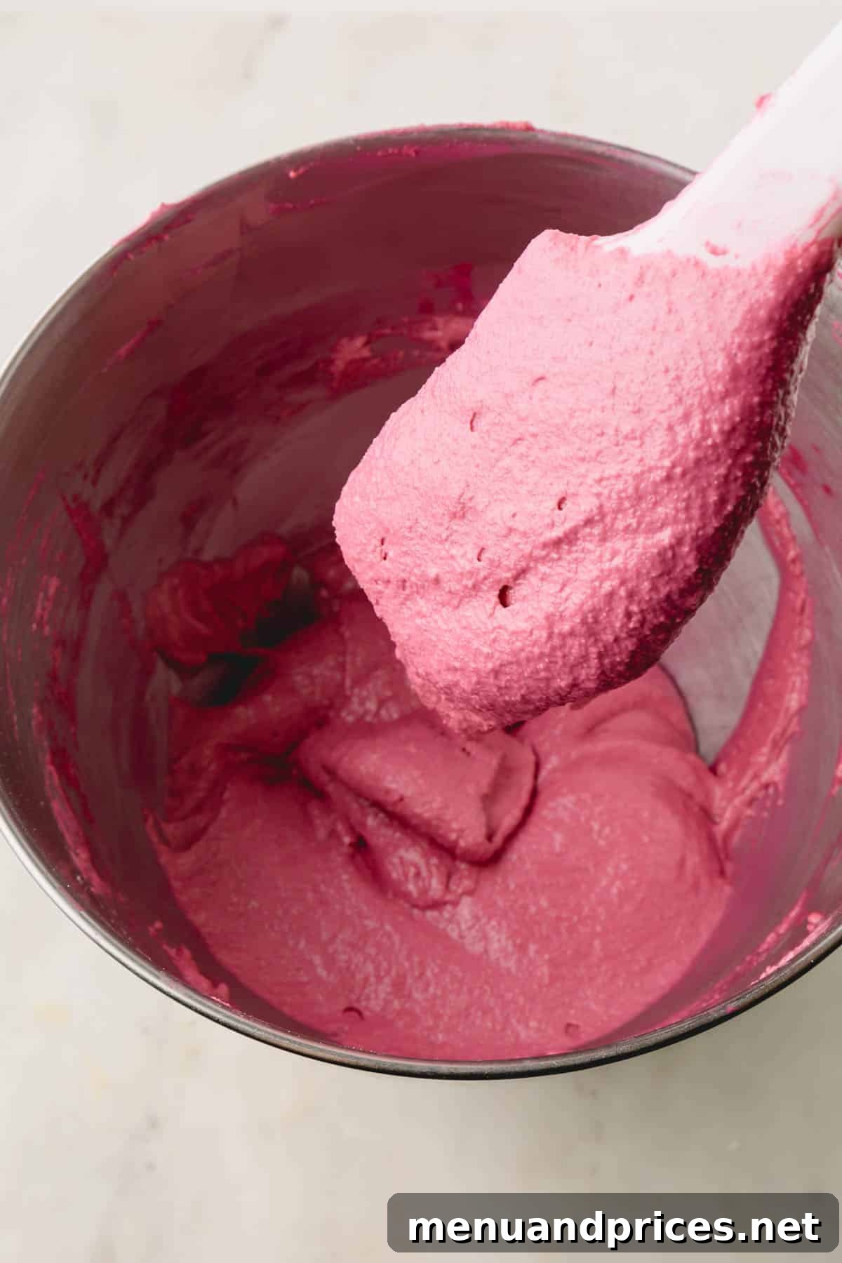 A spatula gently lifting a scoop of vibrant cranberry macaron batter, showing its flowing consistency.