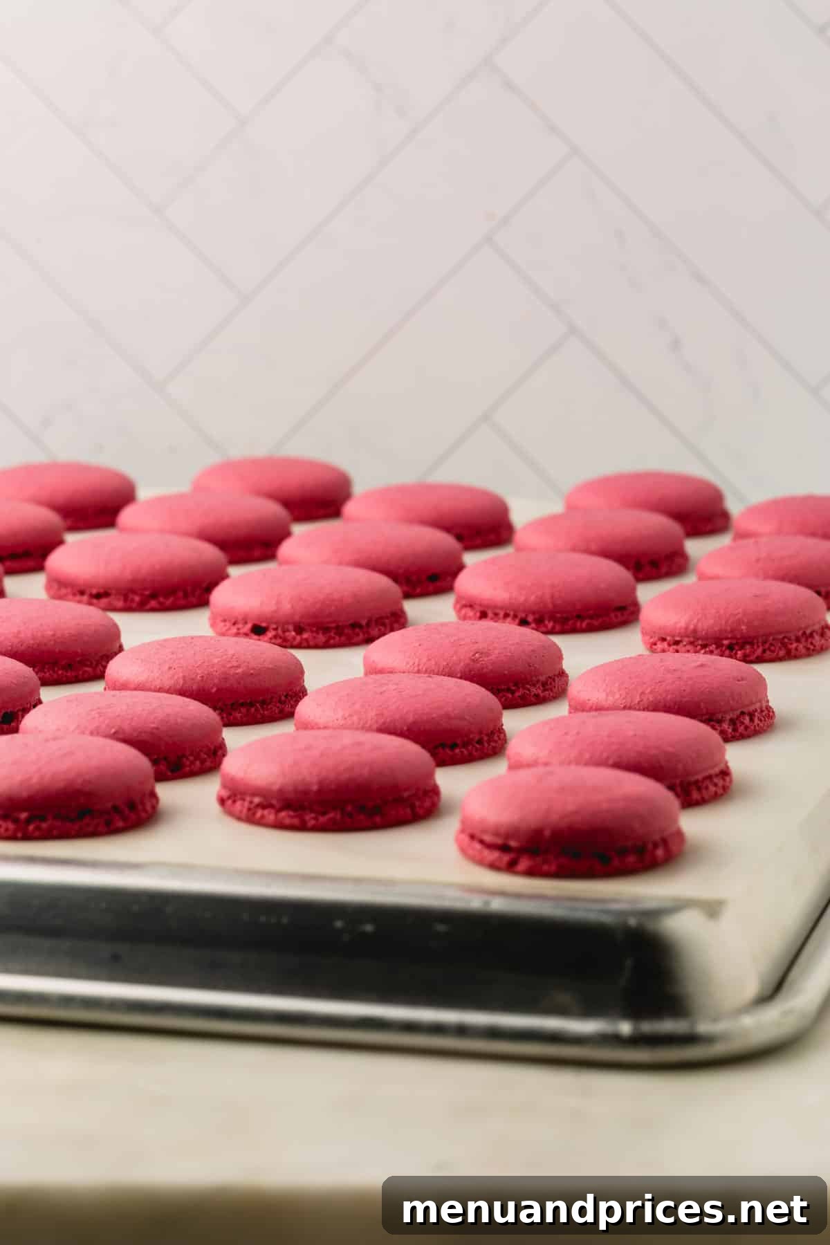 Beautifully baked burgundy macaron shells, showcasing their delicate 'feet', resting on a parchment-lined upside-down baking sheet.