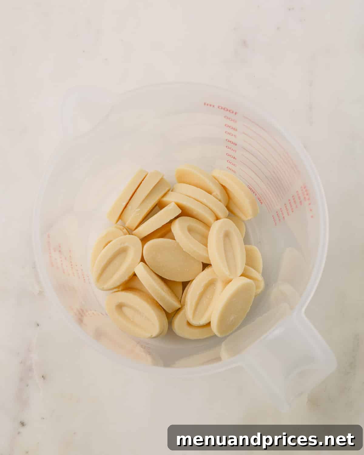 High-quality white chocolate melting wafers in a plastic liquid measuring cup, ready to be melted.