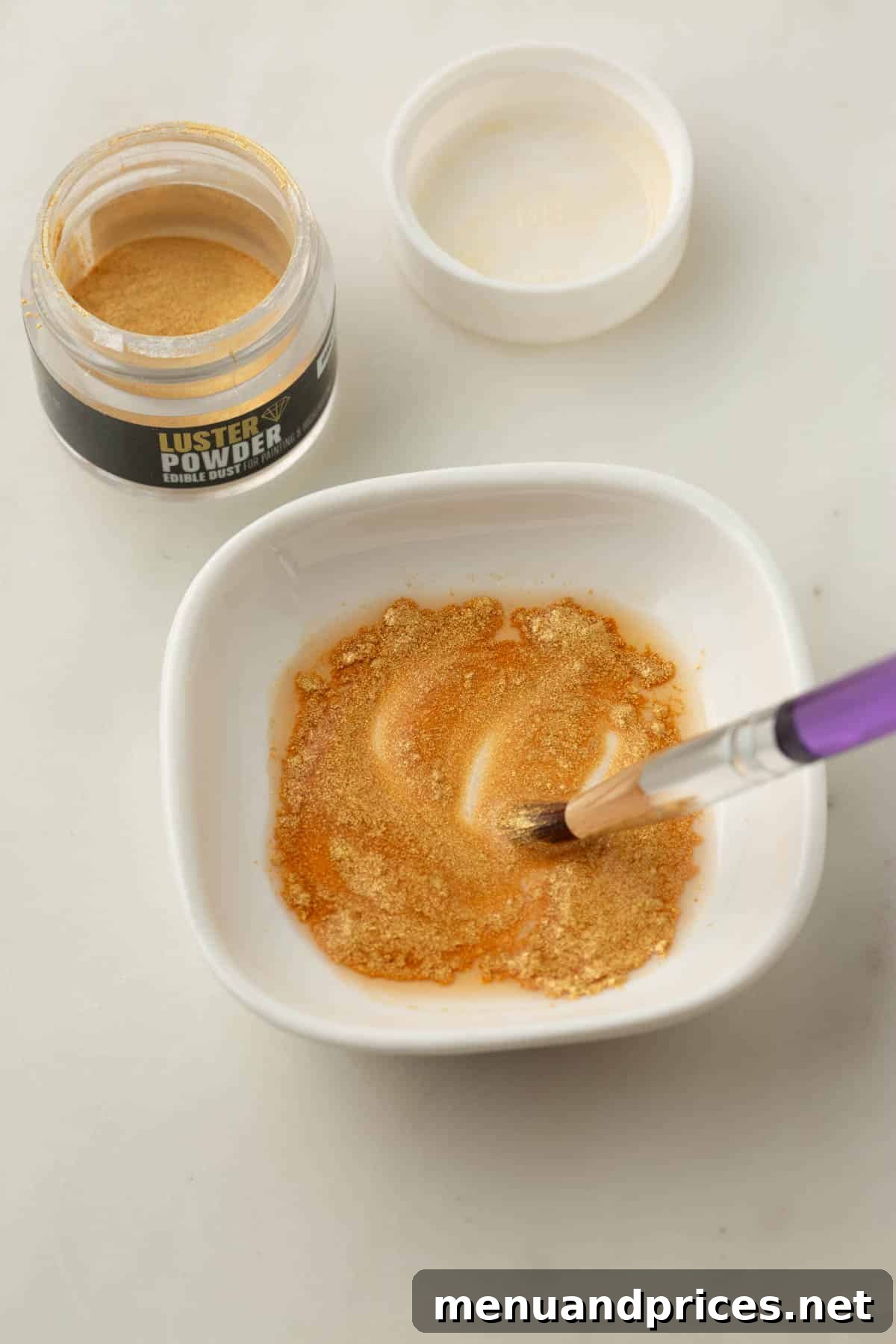A small bowl of edible gold powder, with a paint brush dipping into it, ready for macaron decoration.