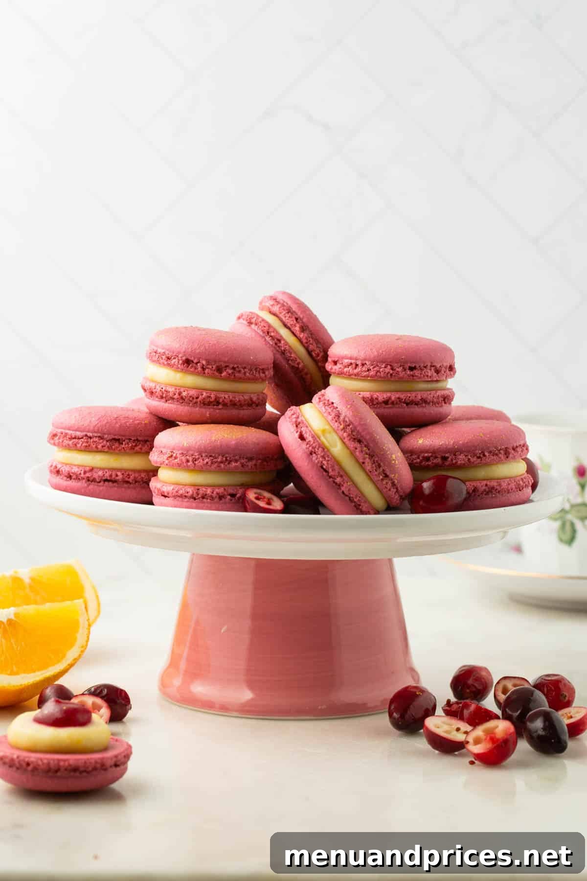 A charming pink cake stand beautifully adorned with perfectly arranged orange cranberry macarons.