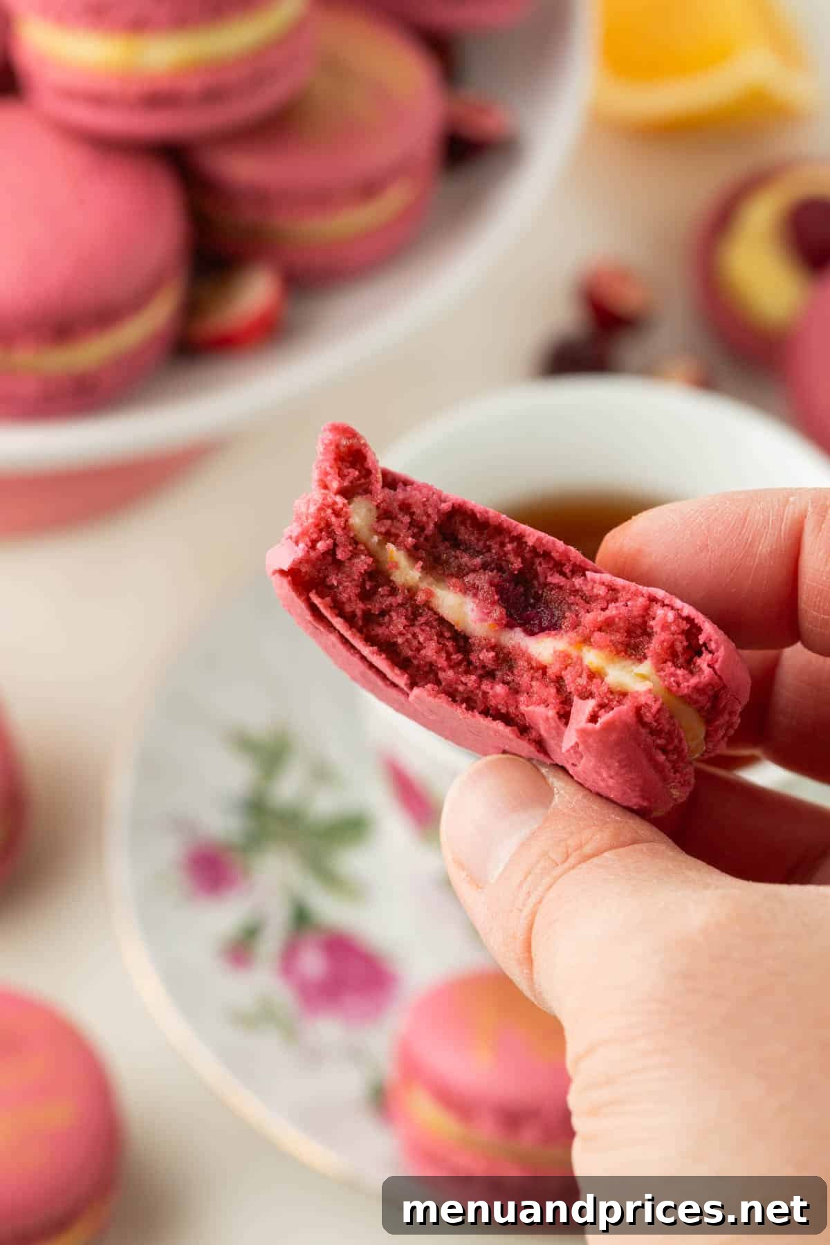 A hand holding an orange meringue and cranberry sauce filled cranberry macaron, with a bite missing, showcasing its delicious layers.