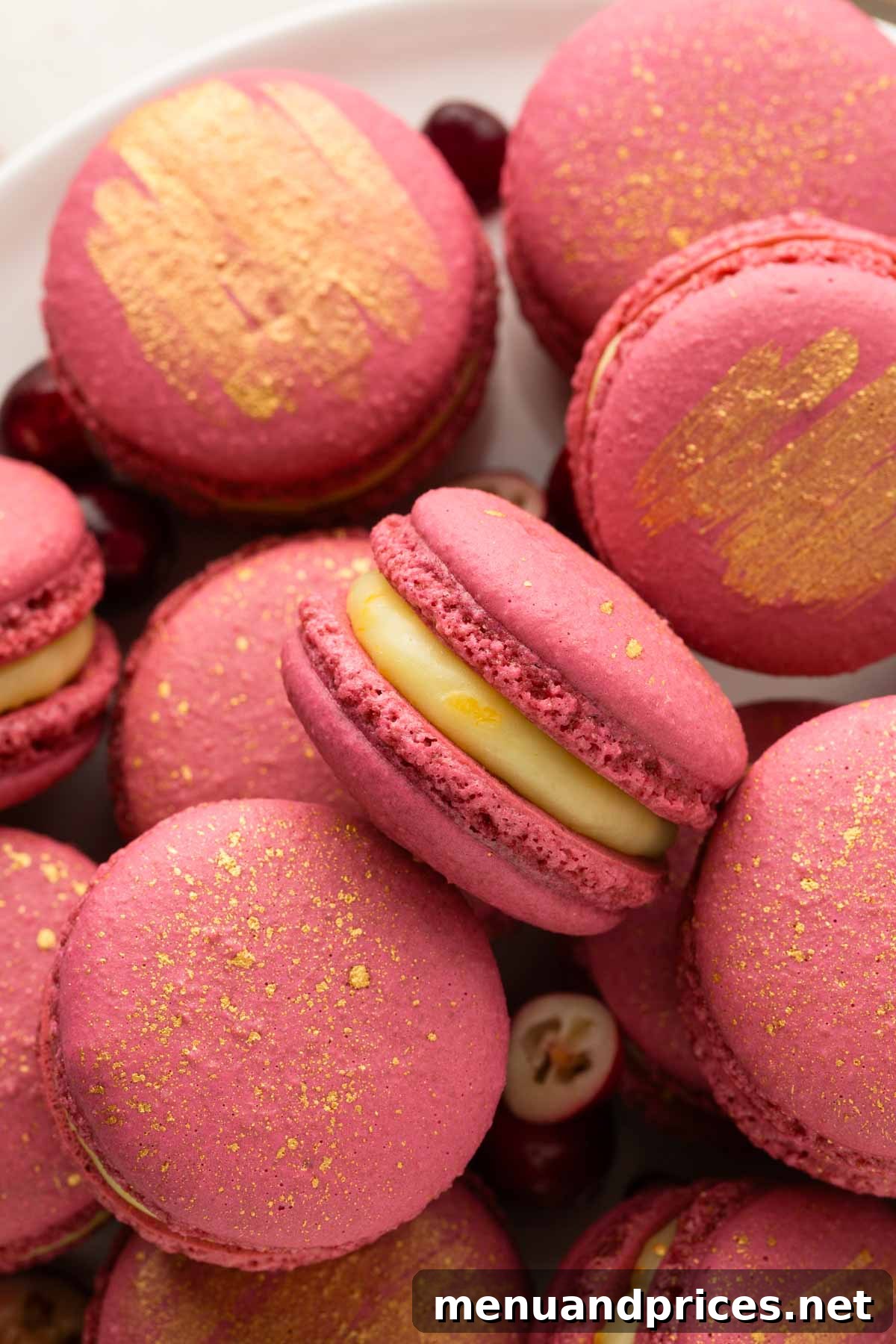 Beautiful pink-orange cranberry macarons delicately dusted with gold, arranged artfully.