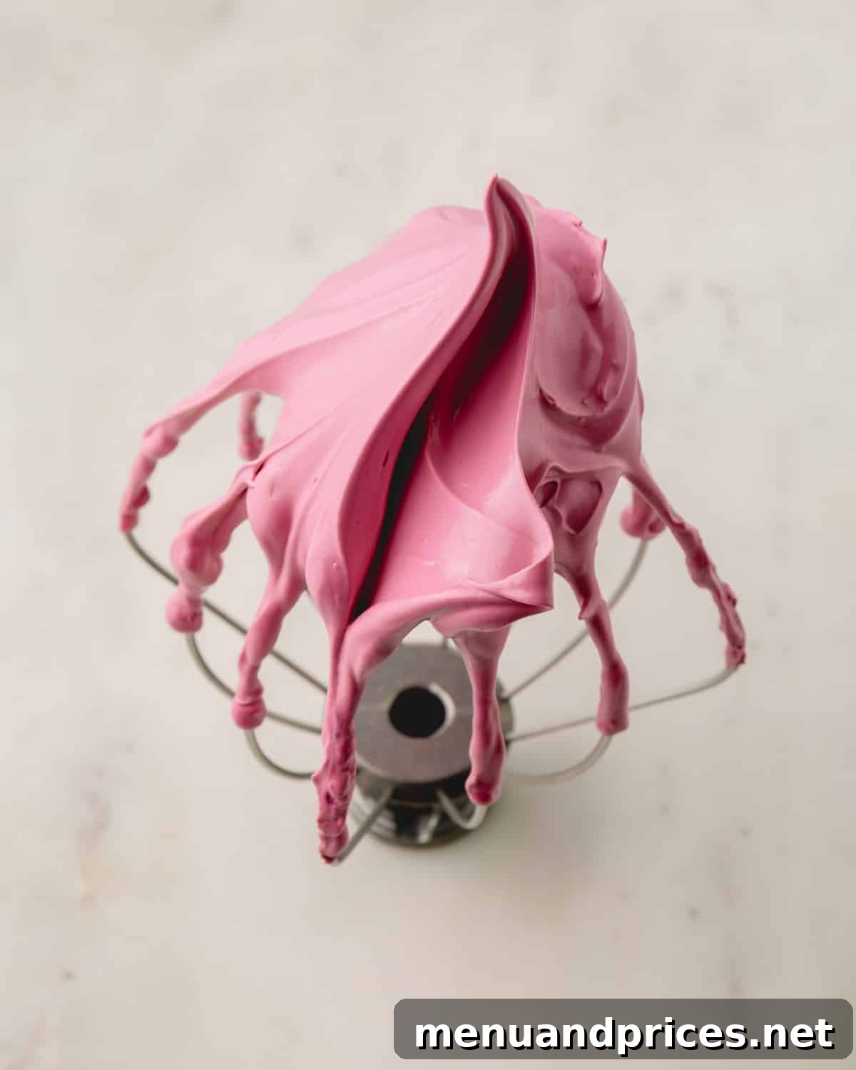 A whisk attachment elegantly displaying perfectly formed, stiff pink meringue peaks.