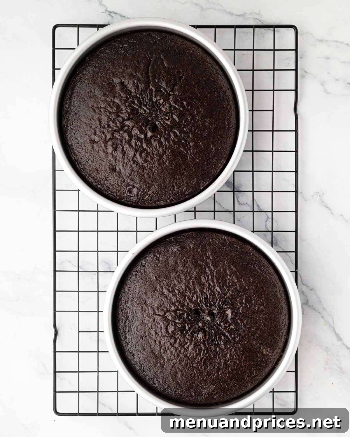 Freshly baked round chocolate cakes resting in their pans on a wire rack to cool.