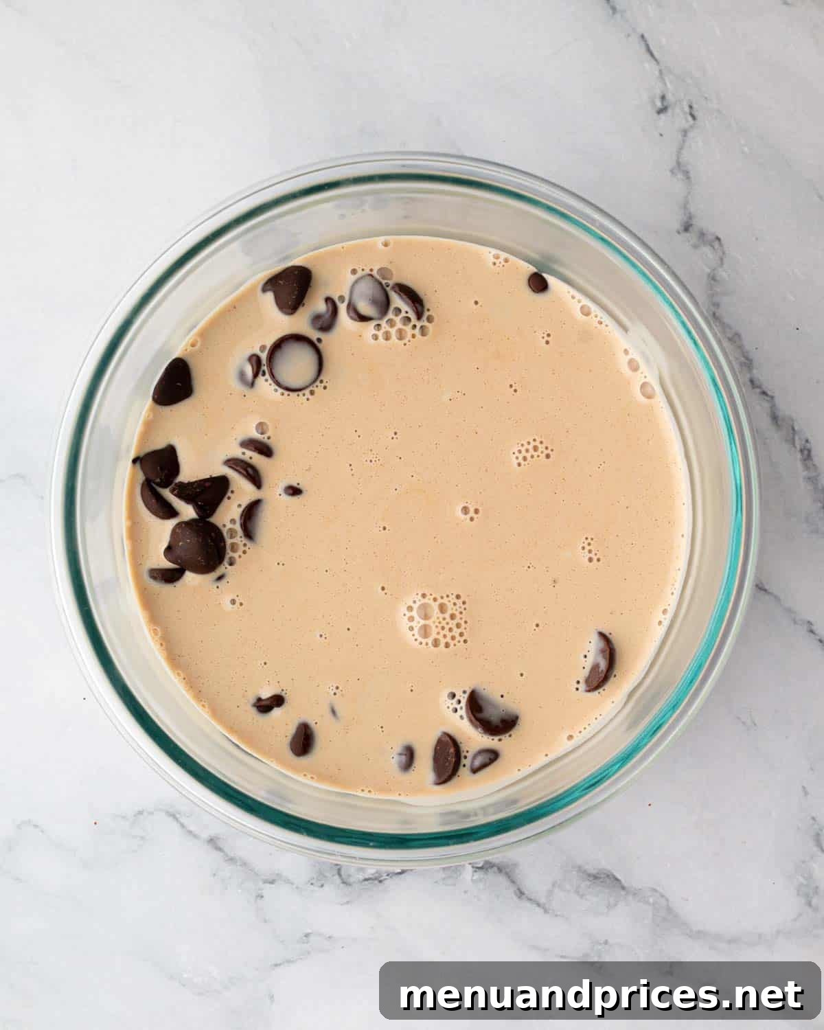 A bowl of finely chopped chocolate covered with hot heavy cream, beginning the ganache process.
