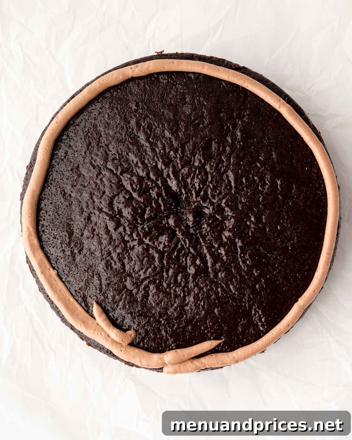 A round chocolate cake with a neat ring of chocolate buttercream piped around its edge, forming a dam.